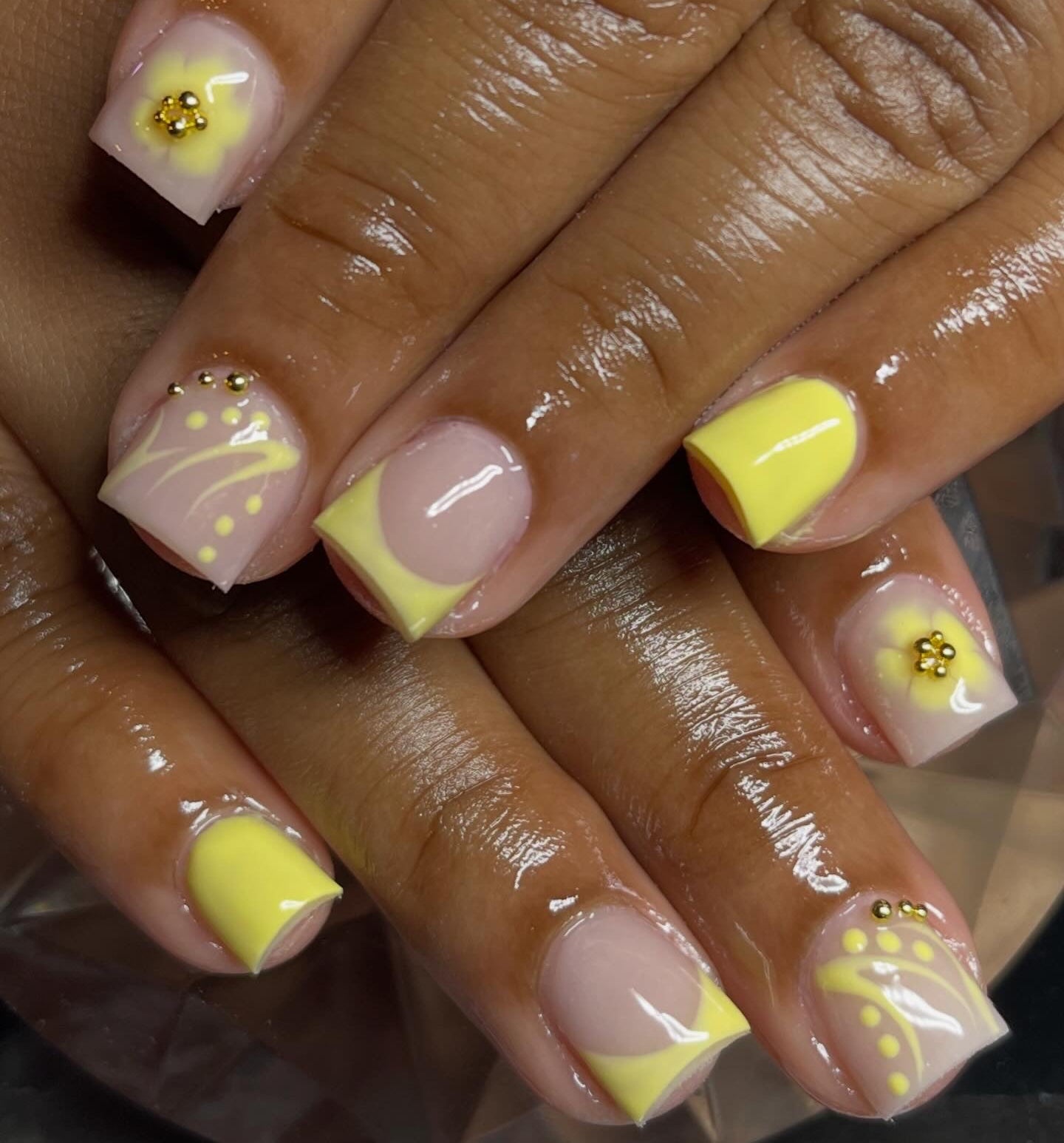 Nails with yellow and pink design on a reflective surface