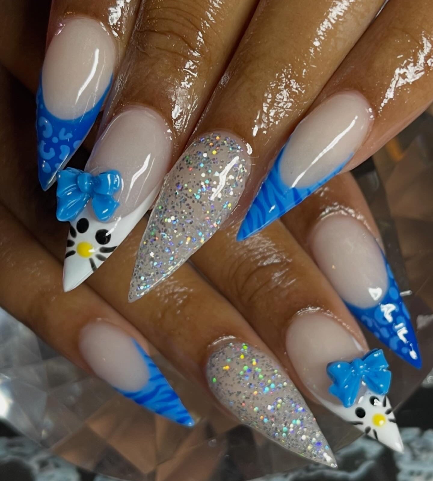 Nails with blue and white designs, including bows and glitter, on a neutral background. hello kitty inspo