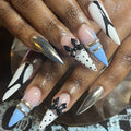 Close-up of hands with decorative nail art featuring bows and metallic accents.