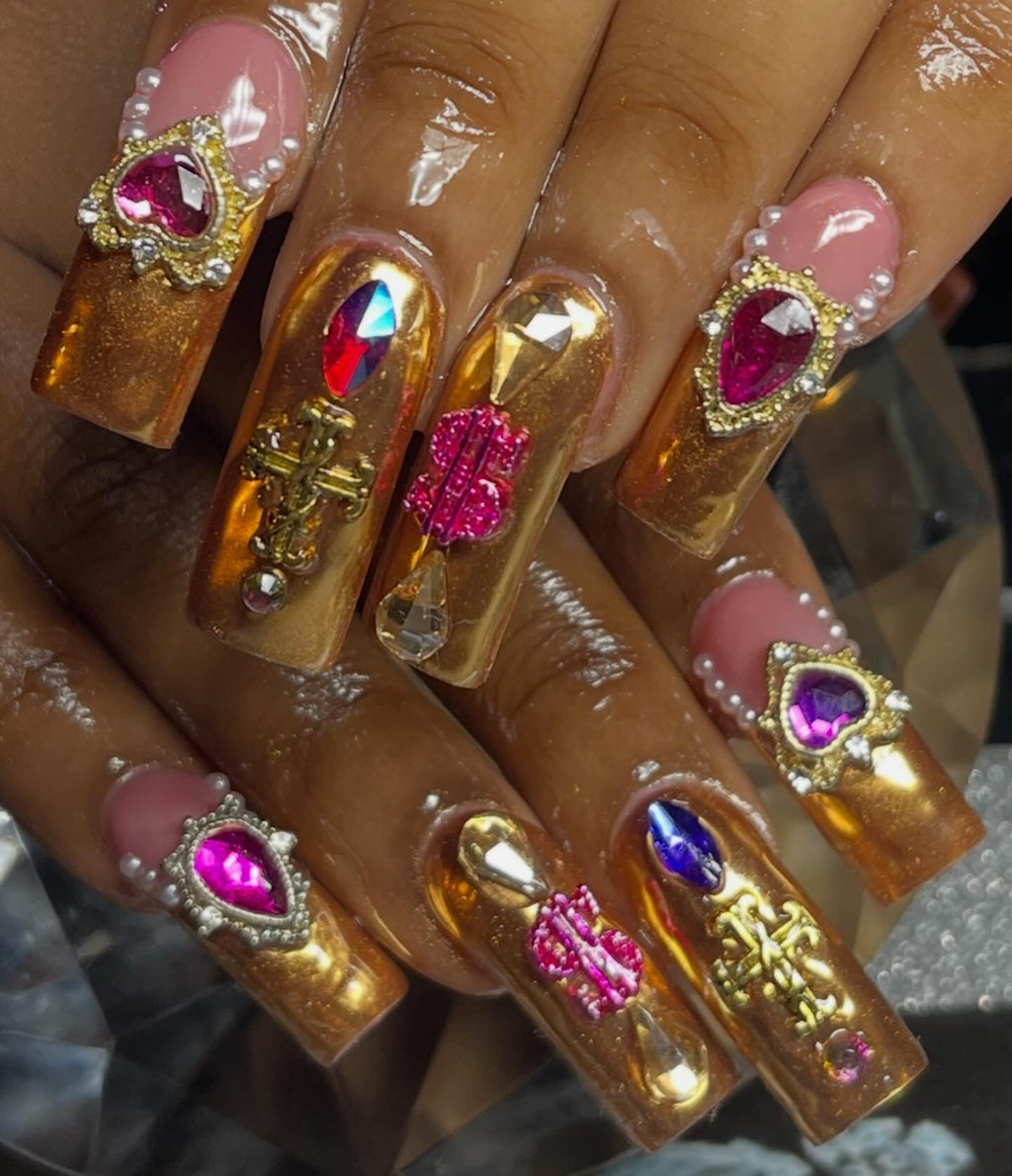 Nails with gold and pink gemstone decorations on a neutral background
