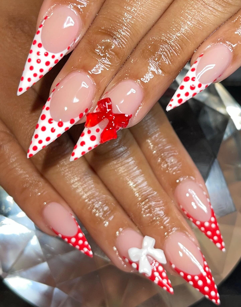 Nails with red and white polka dot design and bow decorations on a reflective surface.