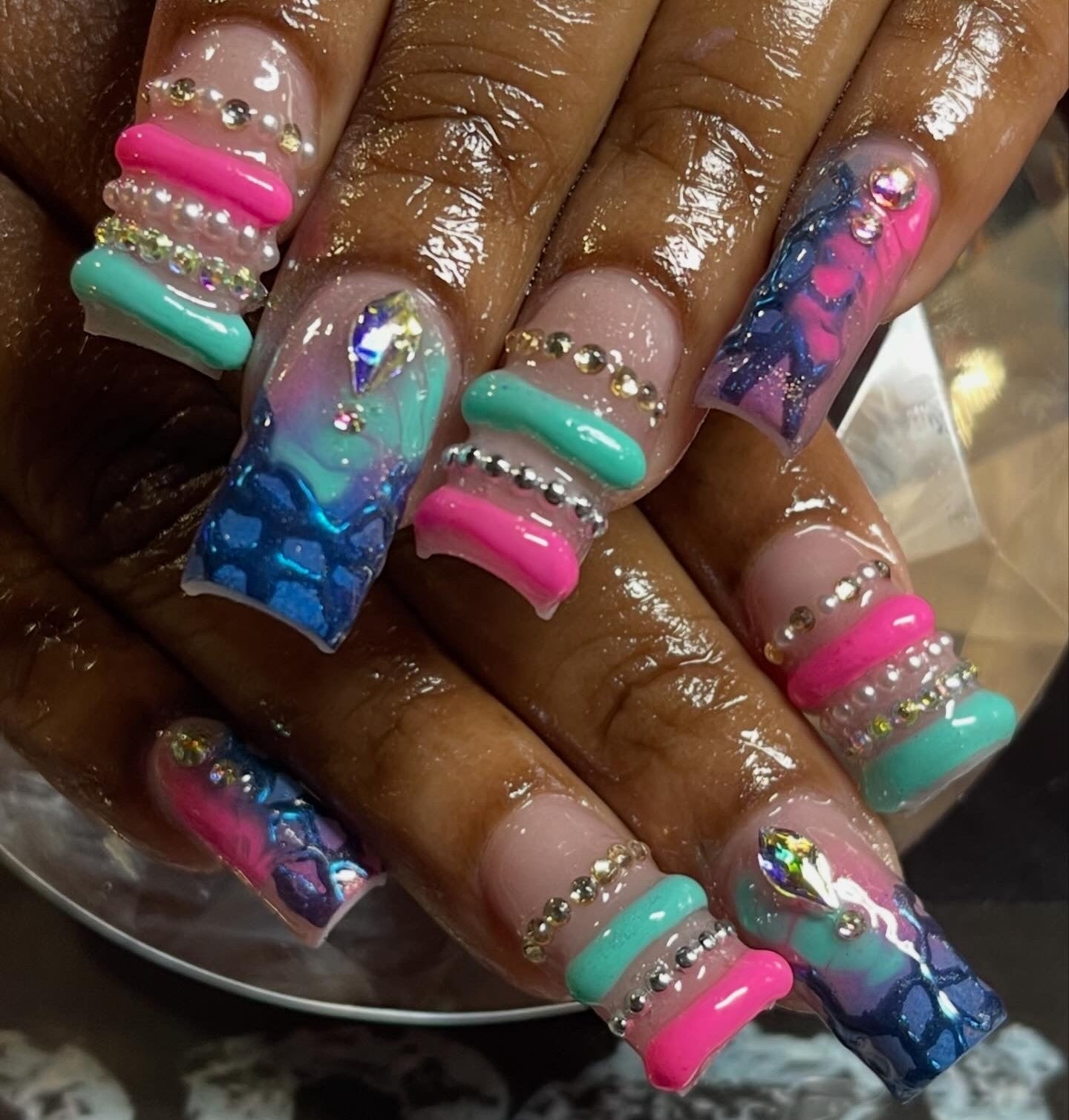 Colorful nail art with turquoise, pink, and blue designs on a hand.